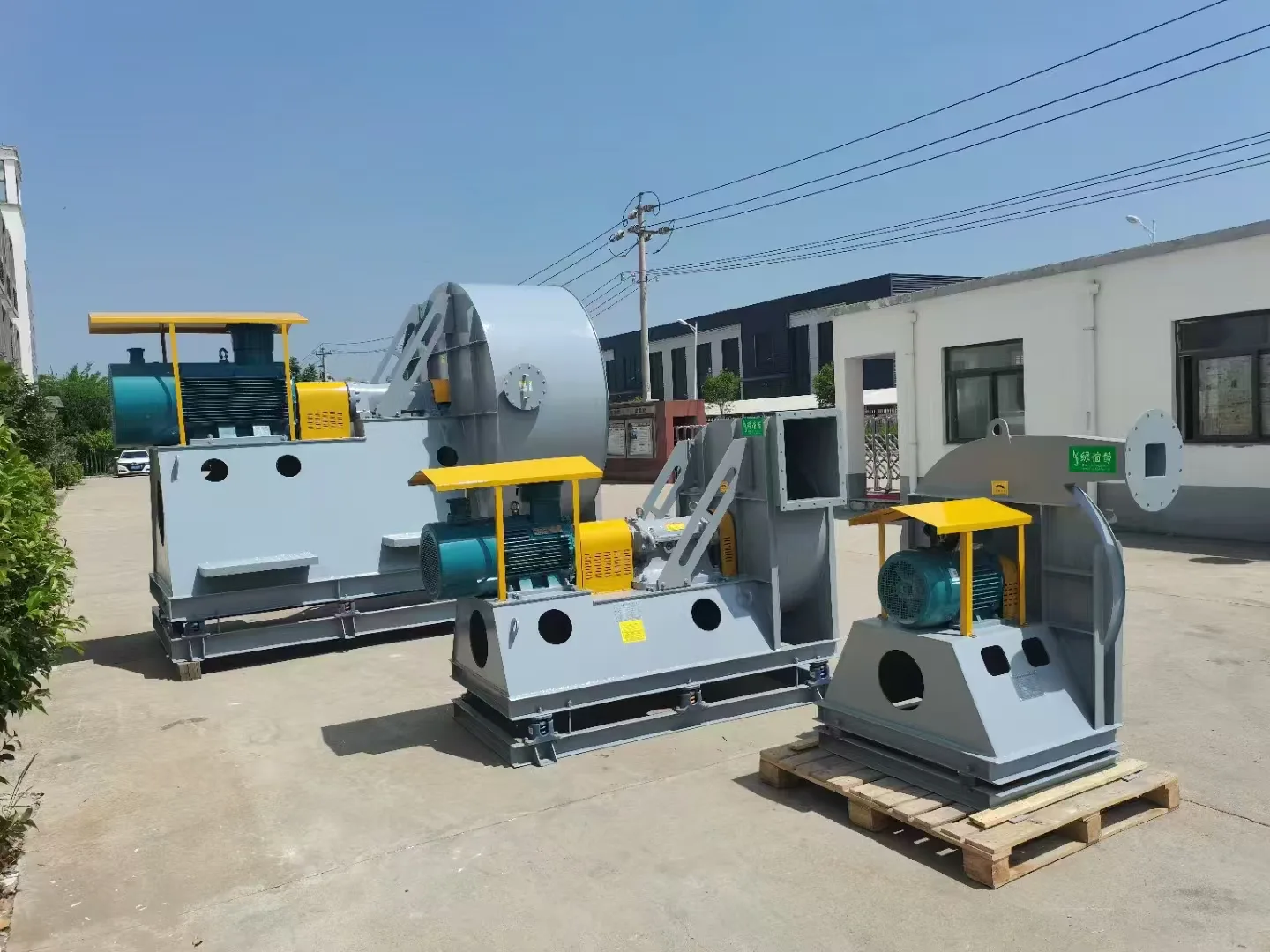 Row of outdoor centrifugal fans with horizontal motors, yellow drive guards and connected metal ductwork